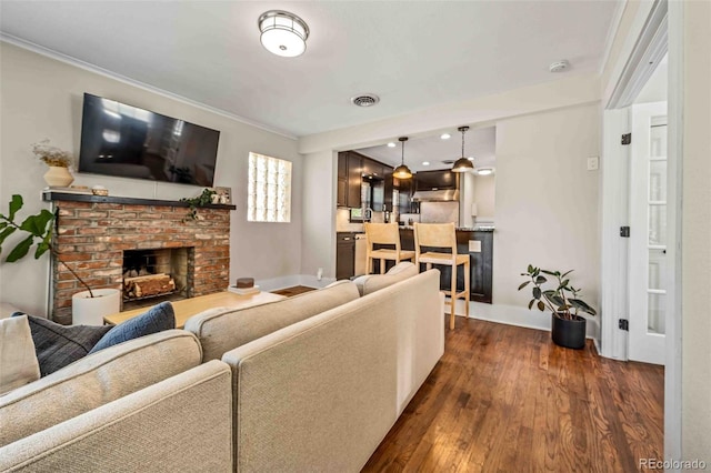 living room featuring dark wood-type flooring, ornamental molding, and a brick fireplace