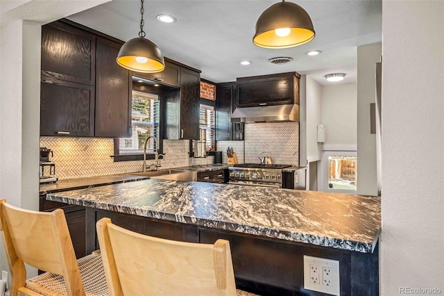 kitchen featuring tasteful backsplash, dark stone counters, hanging light fixtures, exhaust hood, and high end stainless steel range