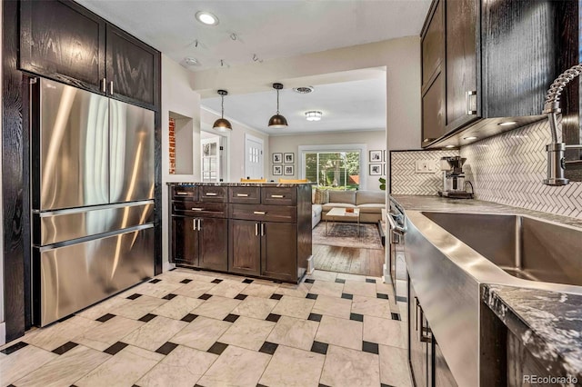 kitchen with pendant lighting, tasteful backsplash, dark stone countertops, stainless steel fridge, and dark brown cabinets