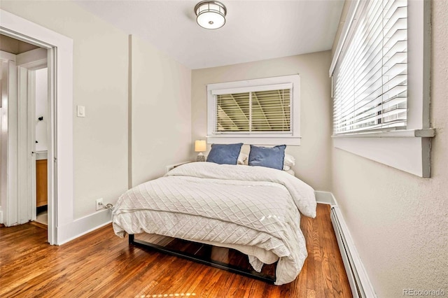 bedroom featuring a baseboard heating unit and hardwood / wood-style flooring