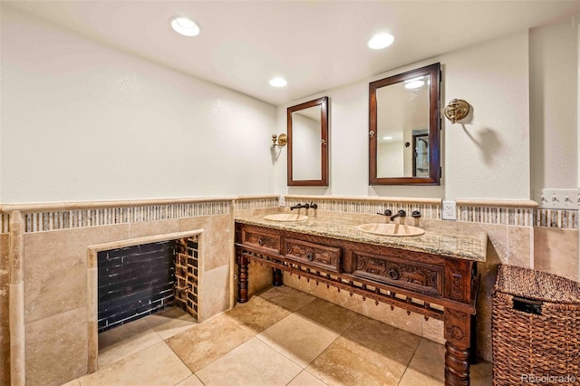 bathroom with a wainscoted wall, a sink, tile walls, and recessed lighting