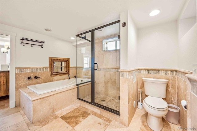 full bath with a wainscoted wall, tile walls, toilet, a stall shower, and a bath