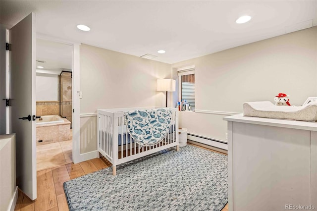 bedroom with a baseboard radiator, light wood-style flooring, a nursery area, and recessed lighting