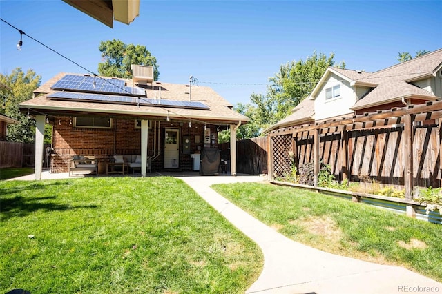 back of house featuring solar panels, a patio, a fenced backyard, a yard, and brick siding