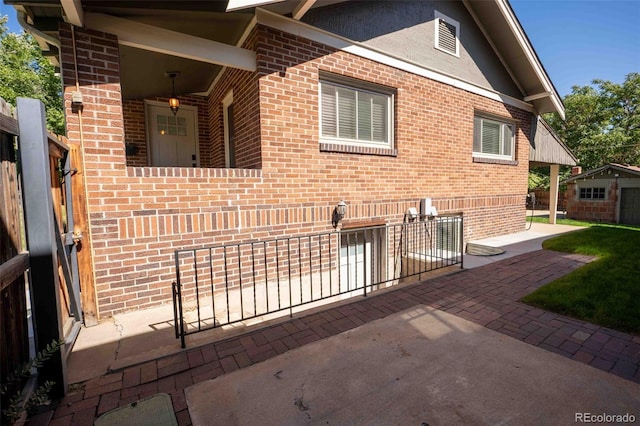 view of property exterior featuring a patio area, brick siding, an outdoor structure, and fence