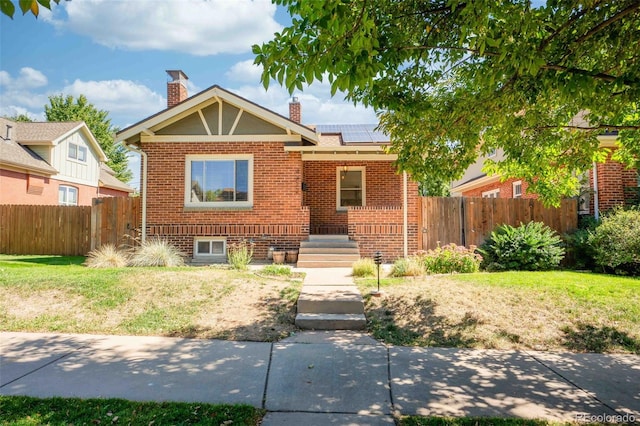 bungalow-style house featuring fence private yard, brick siding, a chimney, and solar panels