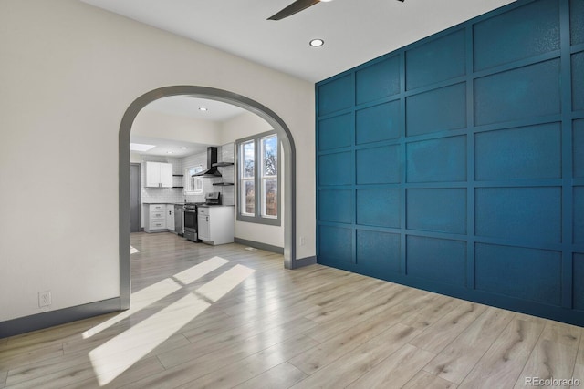 104 Stuart St, Denver, CO 80219 - unfurnished living room with a decorative wall, arched walkways, a ceiling fan, light wood-style flooring, and baseboards