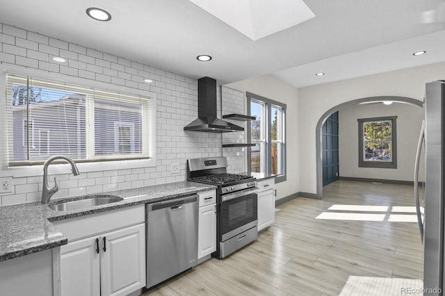 104 Stuart St, Denver, CO 80219 - kitchen featuring appliances with stainless steel finishes, wall chimney range hood, a sink, backsplash, and white cabinetry