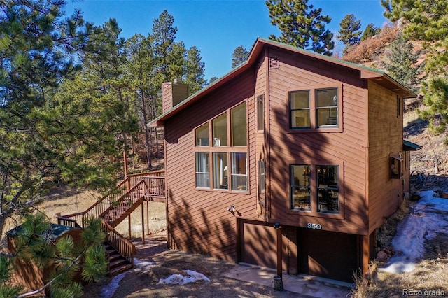 view of side of home featuring stairway, an attached garage, and a chimney
