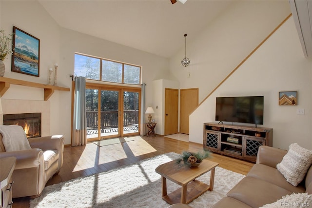 living area featuring ceiling fan, high vaulted ceiling, wood finished floors, and a tiled fireplace