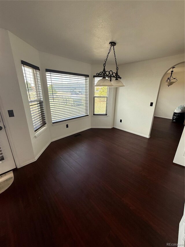 8318 Ivory Loop, Peyton, CO 80831 - unfurnished dining area featuring dark wood-style floors, baseboards, and arched walkways