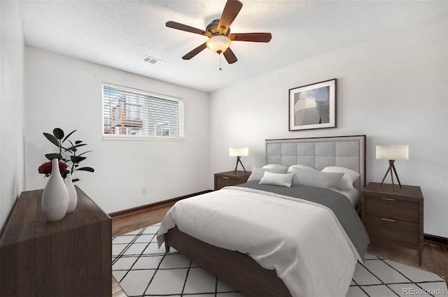 bedroom featuring baseboards, ceiling fan, visible vents, and a textured ceiling