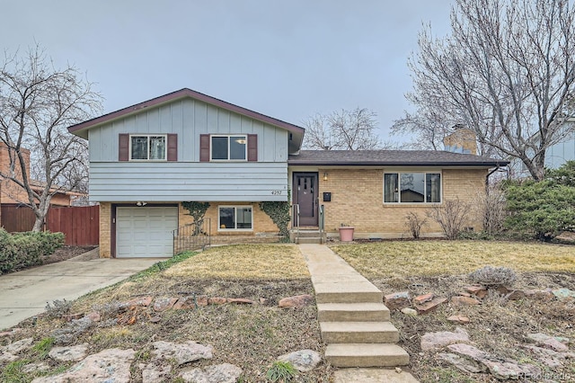 tri-level home with driveway, fence, an attached garage, brick siding, and a chimney