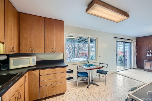 kitchen with dark countertops, brown cabinetry, white microwave, and a sink