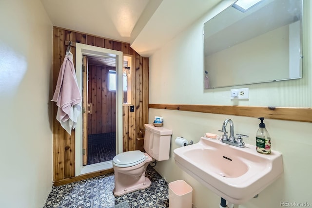 half bath featuring a sink, wooden walls, and toilet