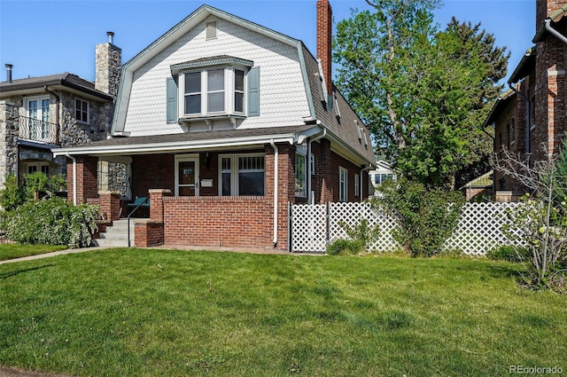 view of front of home with a chimney, covered porch, a front lawn, brick siding, and a gambrel roof
