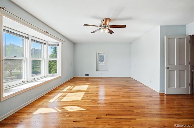 spare room with light wood-type flooring, ceiling fan, and baseboards