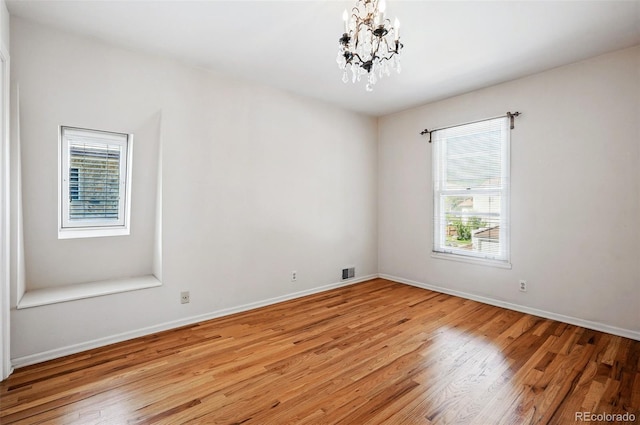 empty room with light wood-style floors, a chandelier, and baseboards