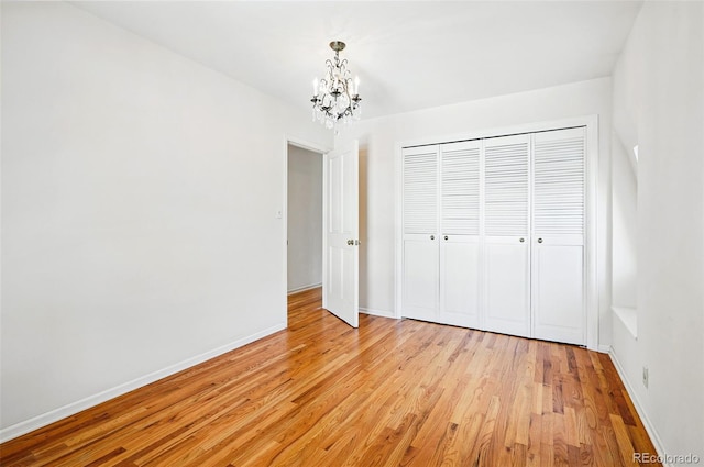 unfurnished bedroom with a chandelier, light wood-type flooring, a closet, and baseboards