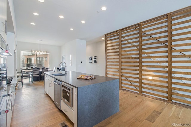 kitchen with an island with sink, white cabinetry, hanging light fixtures, and light wood-type flooring