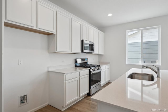 kitchen with sink, white cabinetry, stainless steel appliances, and light hardwood / wood-style flooring