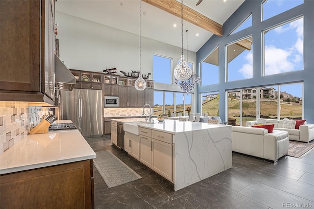 kitchen with tasteful backsplash, stainless steel appliances, sink, beam ceiling, and an island with sink