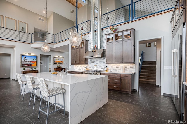 kitchen with dark brown cabinetry, sink, a high ceiling, an island with sink, and pendant lighting