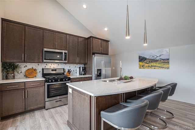 kitchen with light stone countertops, light hardwood / wood-style flooring, pendant lighting, a center island with sink, and appliances with stainless steel finishes