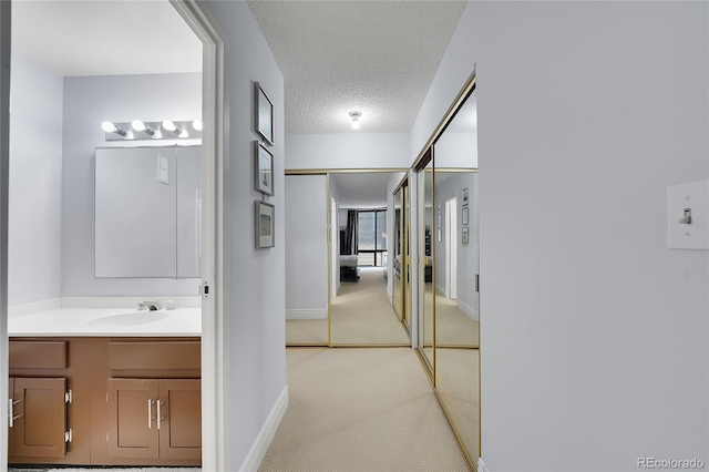 hallway with sink, light colored carpet, and a textured ceiling