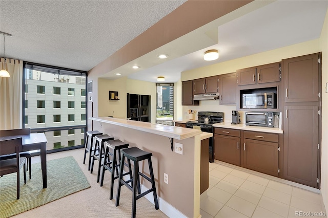 kitchen featuring pendant lighting, a center island, black appliances, a kitchen bar, and dark brown cabinetry