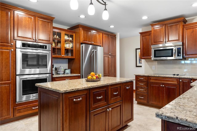 kitchen with light stone countertops, stainless steel appliances, decorative light fixtures, backsplash, and a kitchen island