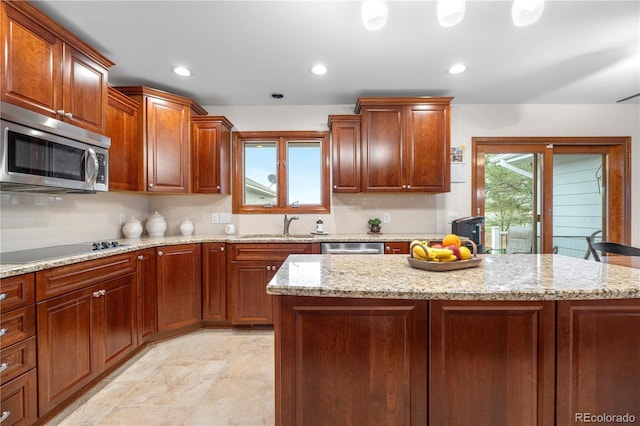 kitchen featuring decorative backsplash, light stone countertops, a sink, stainless steel microwave, and black electric stovetop