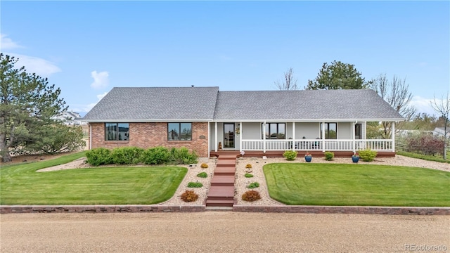 view of front of property with covered porch, brick siding, a front yard, and roof with shingles