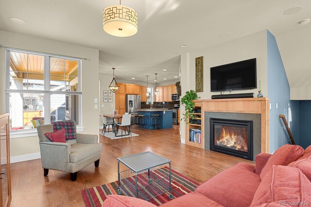 living area featuring recessed lighting, baseboards, wood finished floors, and a glass covered fireplace