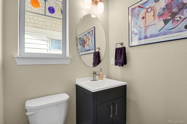 bathroom with a textured wall, vanity, and toilet