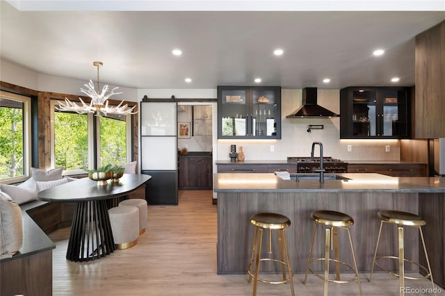 189 Pine Cone Ln, Winter Park, CO 80482 - kitchen featuring wall chimney exhaust hood, light wood-style floors, decorative backsplash, dark countertops, and a barn door