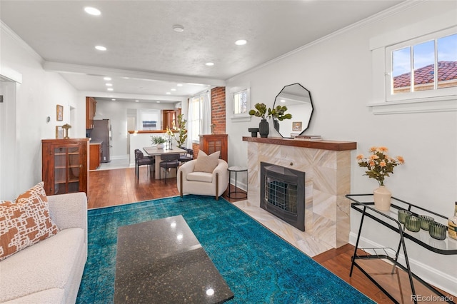 living room with ornamental molding, wood-type flooring, and a tiled fireplace