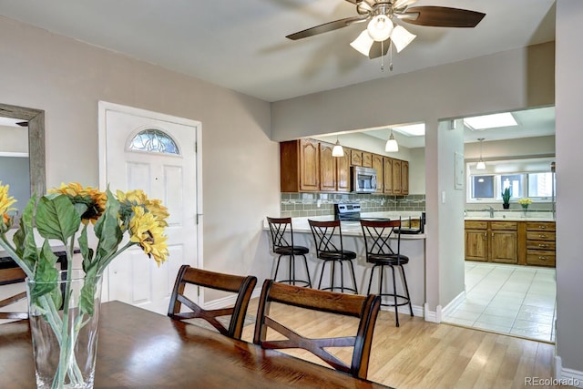 kitchen featuring stainless steel appliances, brown cabinets, decorative backsplash, a breakfast bar area, and ceiling fan