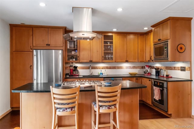 kitchen featuring island exhaust hood, light hardwood / wood-style flooring, a center island, a kitchen bar, and appliances with stainless steel finishes