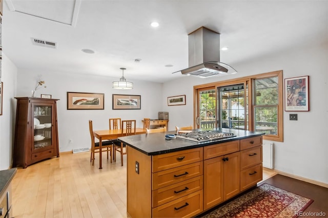 kitchen with island exhaust hood, hanging light fixtures, stainless steel gas cooktop, a center island, and light hardwood / wood-style floors