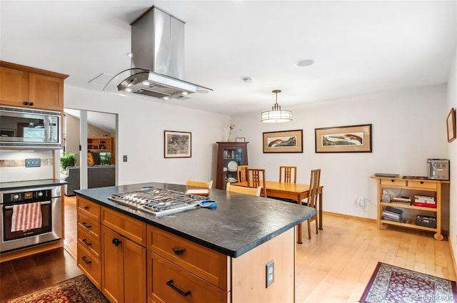 kitchen with island exhaust hood, hanging light fixtures, appliances with stainless steel finishes, light wood-type flooring, and a center island