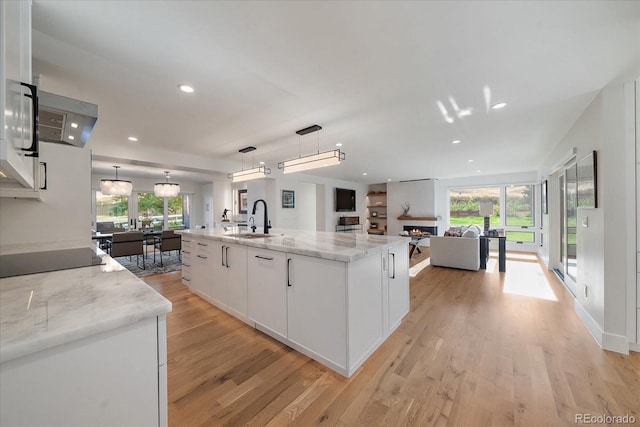 kitchen with light stone counters, pendant lighting, sink, white cabinetry, and a spacious island