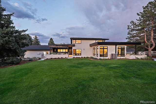 back house at dusk with a pergola, central AC, a patio area, and a yard