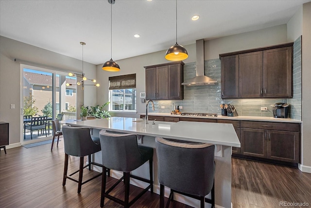 kitchen featuring a center island with sink, stainless steel gas cooktop, hanging light fixtures, and wall chimney exhaust hood