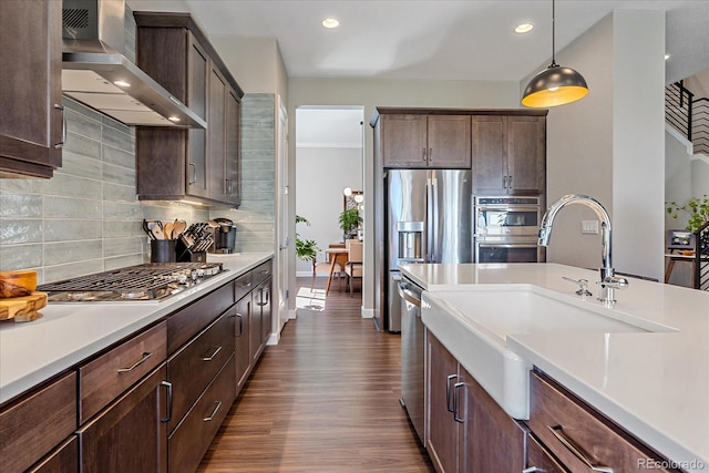 kitchen with appliances with stainless steel finishes, hanging light fixtures, sink, wall chimney range hood, and tasteful backsplash