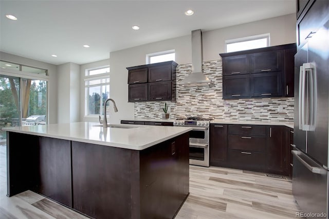 kitchen featuring appliances with stainless steel finishes, wall chimney exhaust hood, a healthy amount of sunlight, and an island with sink