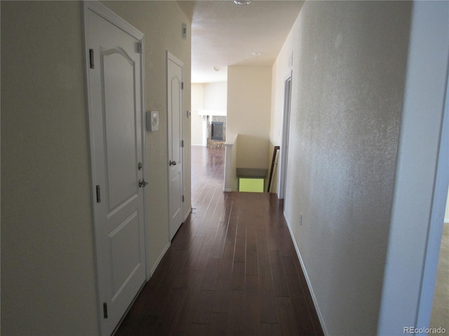 hall featuring baseboards, dark wood finished floors, and a textured wall