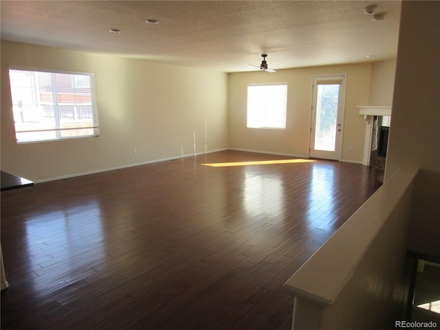 unfurnished living room featuring dark wood-style floors, a textured ceiling, a ceiling fan, and a tiled fireplace