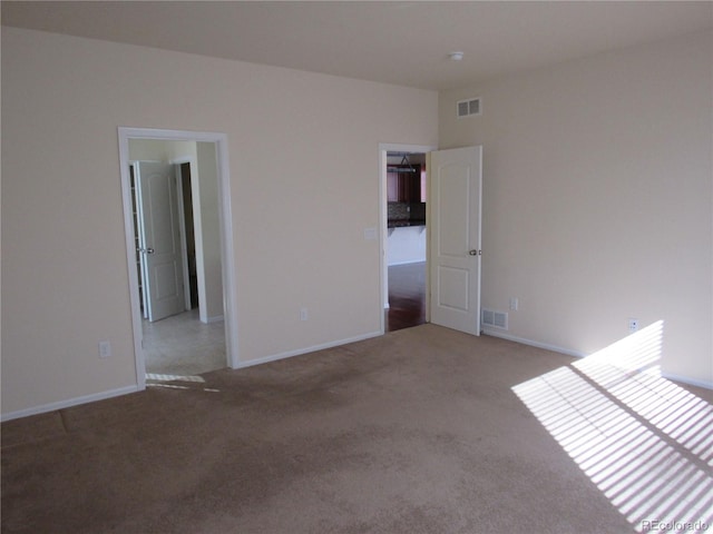 empty room with carpet, visible vents, and baseboards