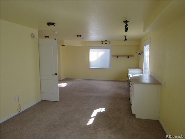 spare room with baseboards, light carpet, and track lighting